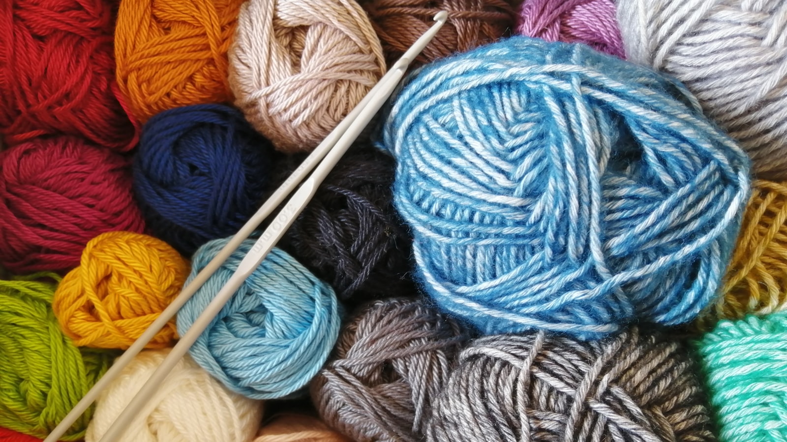 Hands casting stitches onto a wooden knitting needle with soft pale yarn.