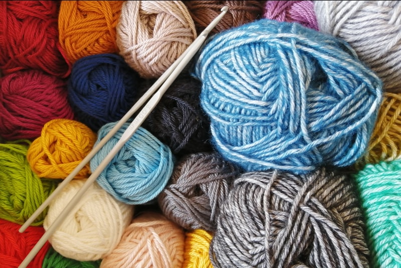 Hands casting stitches onto a wooden knitting needle with soft pale yarn.